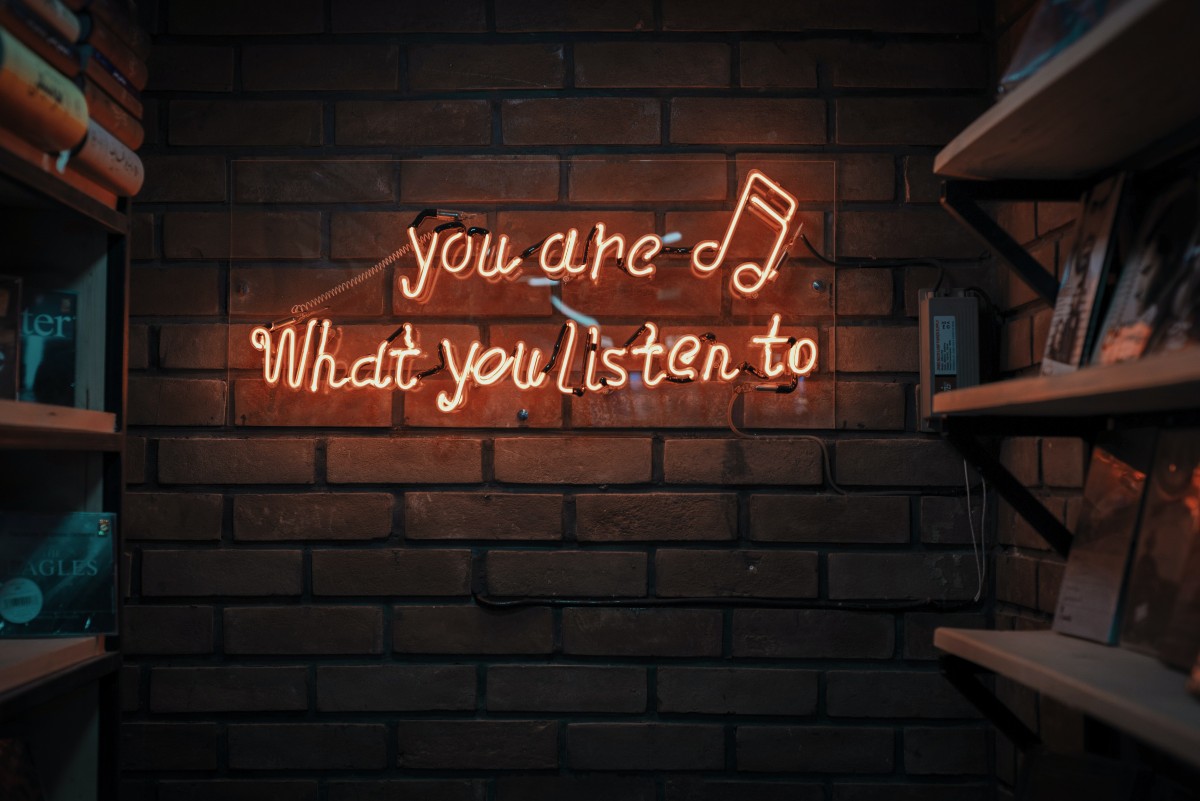 A brick wall with a red neon sign that says "you are what you listen to"