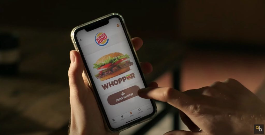 A screenshot from Burger King's commercial showing a person clicking "order delivery" on Burger King's app 