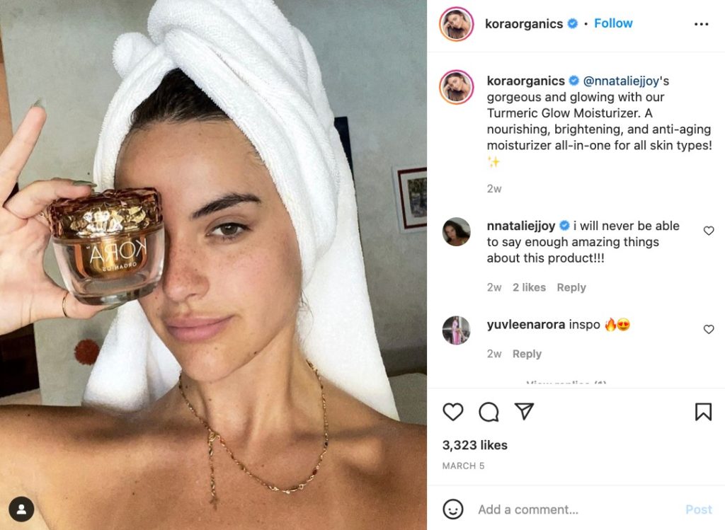 A selfie of a woman wearing a towel on her head as she shows off her Kora Organics product